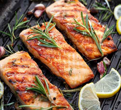 Grilled salmon fillets sprinkled with fresh herbs and lemon juice on a grill plate close up 