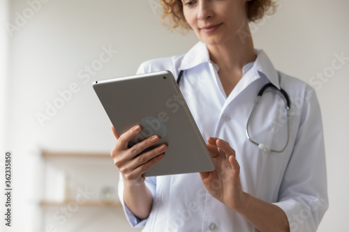 Crop close up of female doctor hold tablet fill patient medical history anamnesis online, woman nurse or GP use pad gadget, consult client on internet, browse results on device, technology concept