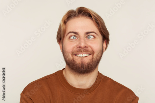 Closeup portrait of idiot, dumb bearded man looking cross-eyed with stupid smile, fooling around, making silly face, brainless comical expression. indoor studio shot isolated on gray background