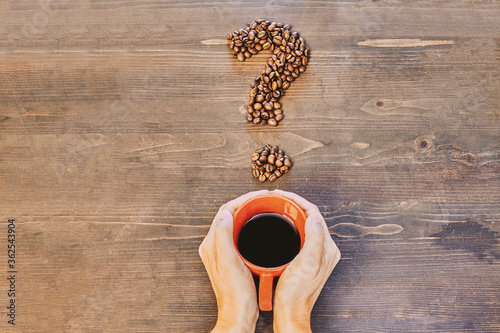 Hands holding a red coffee cup on a wooden table and with a question mark made of coffee beans