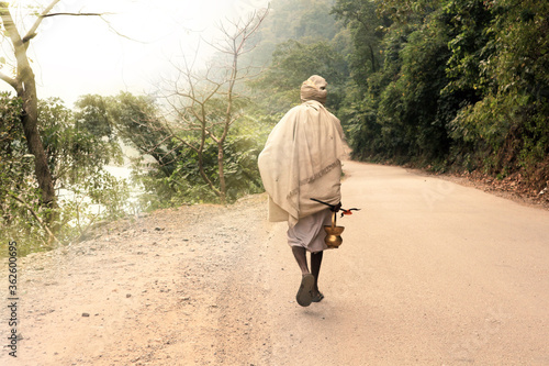 Indian renounced sadhu leaves on the way to the forest. A wandering wanderer with a trident and a kamandala. Photo from the back.