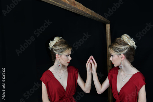 beautiful girl in evening burgundy dress by the mirror with her reflection on a black background