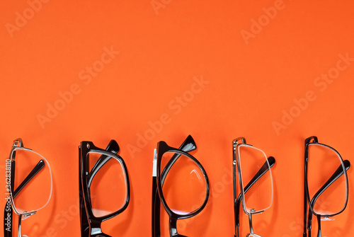Different types of glasses on an orange background close up. Glasses with rectangular and round frames. Layout for design. Space for text and free space near the object.