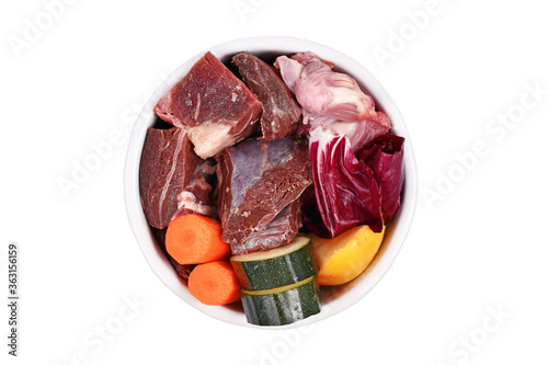 Bowl with species appropriated raw food for dogs like chunks of meat, chicken stomache and vegetabls like carrots, lettuce and zucchini and banana fruits on white background