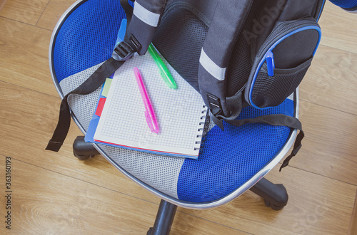 School backpack and notebook with felt-tip pens on a chair. Back to school, education concept.