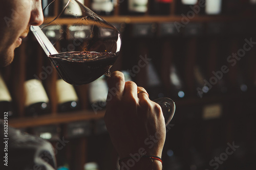 Close-up shot of young sommelier smell red wine on wine cellar background.