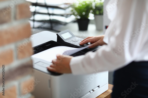 Woman in office prints documents on printer. Scanning documents at workplace concept
