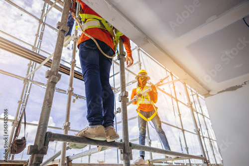 Construction workers in safety uniform install reinforced steel scaffolding at outdoor construction site.