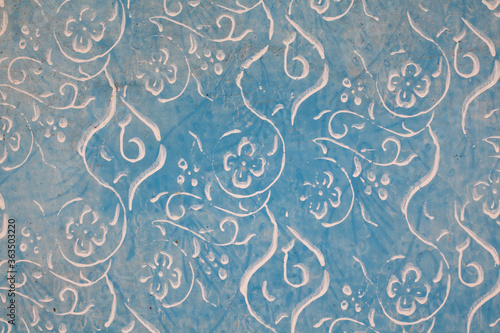 Fragment starej, niebieskiej, wyblakłej ściany, pomalowany farbą kredową , ozdobiony kwiecistym wzorem.