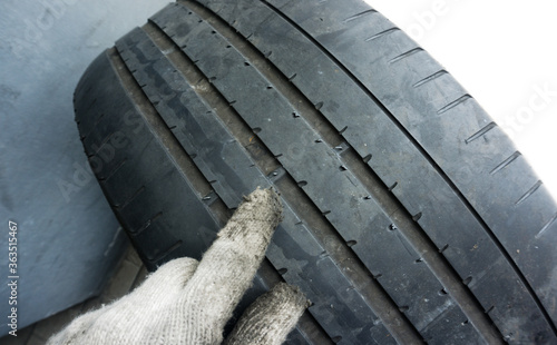 Finger in glove of mechanic pointing at tyre tread wear indicators, Tread wear indicators, built into the main tread grooves, show the tread depth. 