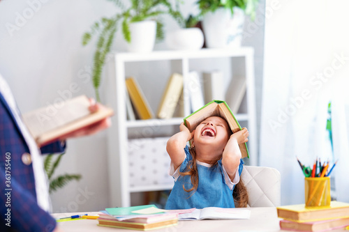 little girl engaged in lessons with teacher at home, fools around and laughs.