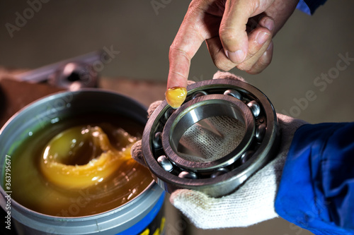 Mechanic is putting lubricant grease into ball bearing in a factory.