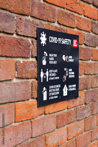 COVID 19 safety information sign for shoppers mounted on brick wall leading to town centre shopping area with shallow depth of field