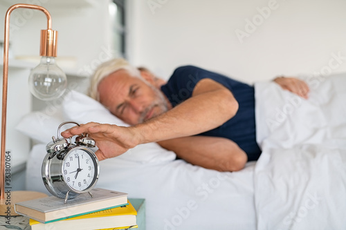 Mature man turning off alarm clock