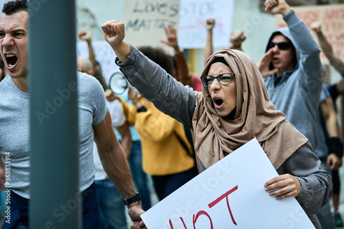 Displeased Muslim woman with raised fist shouting on anti-racial demonstrations.