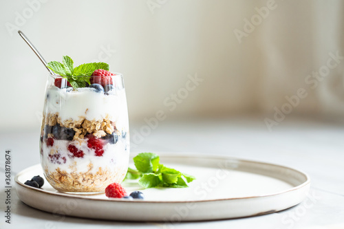 Glass of parfait made of granola, berries and yogurt on the table. Shot at angle with place for text, selective focus.