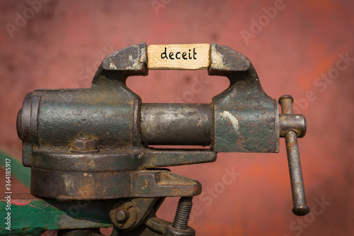 Vice grip tool squeezing a plank with the word deceit