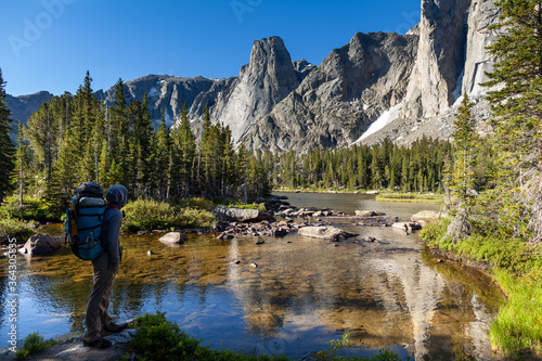 A male backpacker traveling on the North Fork Trail pauses along the North Popo Agie River to take in the view of a lake and cirque on the north side of Big Sandy Mountain in the Wind River Range, WY.