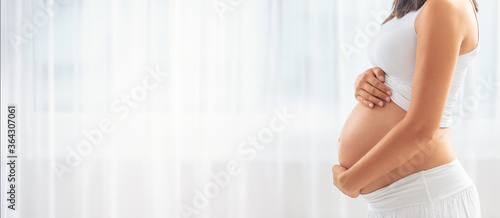 Detail of a pregnant woman dressed in white clothes, with both hands holding the belly