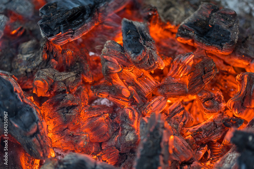 Flame incinerates firewood and transforms it ashes, close up, shallow depth of field. Blaze in a large stove. Nature texture of fire. The flame of fire burns in the brazier, smoldering firewoods.