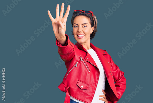 Young beautiful woman wearing red leather jacket showing and pointing up with fingers number four while smiling confident and happy.