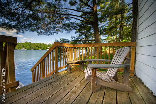 Adirondack chair sitting on a cottage wooden deck facing a calm lake during a summer day in Muskoka, Ontario Canada.