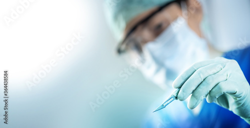 close up of the surgeon's hand holding a scalpel and blurred female doctor's face in the background with copy space, concept of surgical operations, hospitals and clinics staff