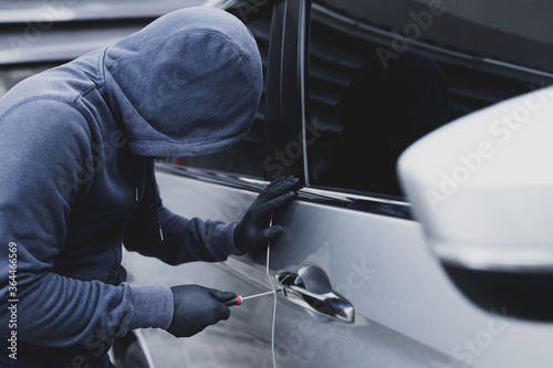 Close up car thief hand holding screwdriver tamper yank and glove black stealing automobile trying door handle to see if vehicle is unlocked trying to break into inside. 