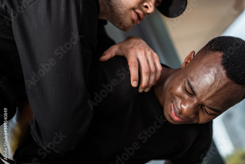 policeman detaining african american man suffering from pain, racism concept