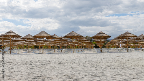 Holidays on the seaside. Empty sandy beach with sun beds and straw parasols waiting for vacationers. Sardinia, Italy.