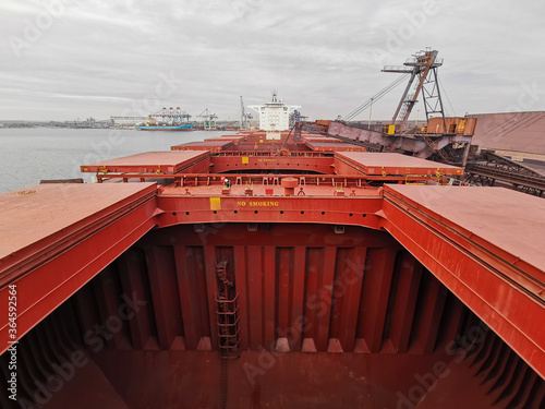 View of bulk carrier main deck with opened hatch-covers, cargo holds during loading of iron ore concentrate in bulk