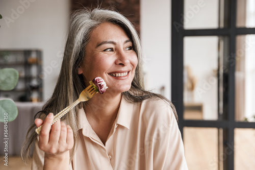 Woman sitting at kitchen indoors at home while eating salad.