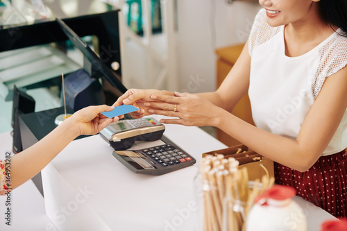 Smiling young woman using credit card when paying for order in cafe