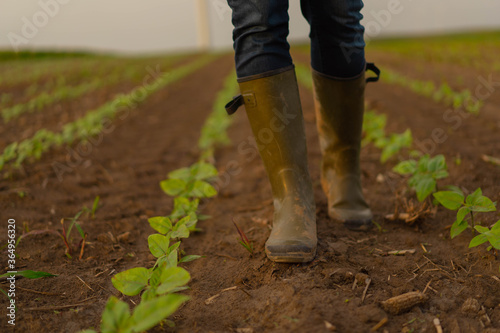 A farmer walks across a field in rubber boots .