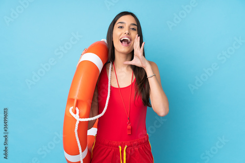 Lifeguard woman over isolated blue background with lifeguard equipment and shouting with mouth wide open