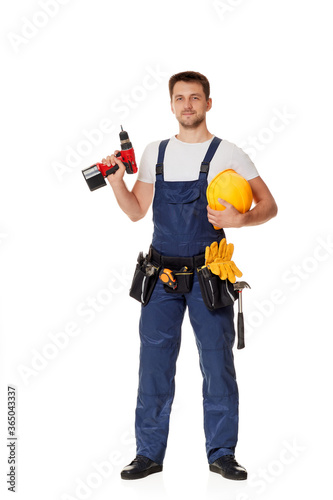 caucasian repairman worker in uniform holding yellow hard hat and cordless screwdriver. handyman wearing tool belt isolated on white studio background