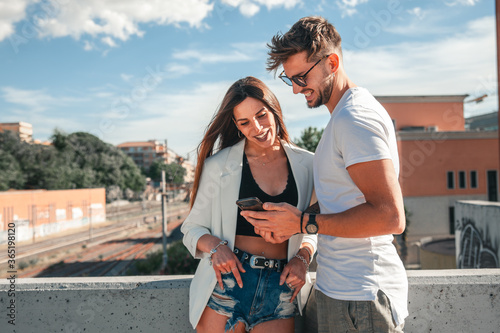 Giovane coppia di innamorati guardano insieme il contenuto del loro telefono con aria allegra e sorridente in una giornata di bel tempo estivo