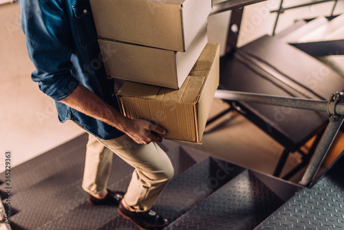 partial view of businessman holding carton boxes and walking on stairs in office