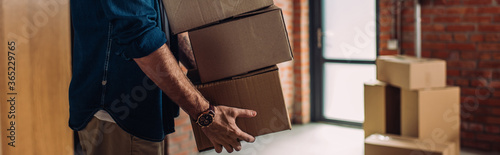 panoramic crop of businessman holding boxes and moving in new office