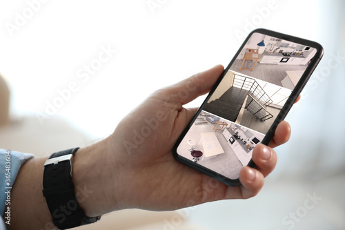 Man monitoring modern CCTV cameras on smartphone indoors, closeup. Home security system