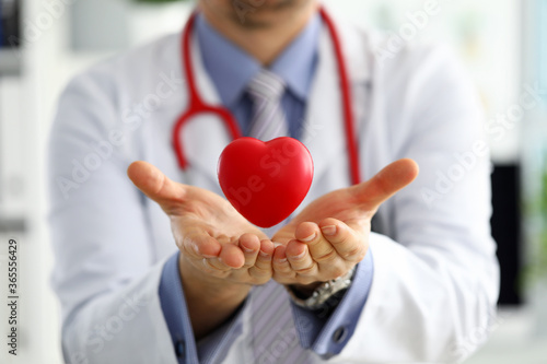 Male medicine doctor hands holding and covering red toy heart