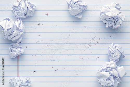 School supplies of blank lined notebook paper with eraser marks and erased pencil writing, surrounded by more trashed balled up paper. Studying or writing mistakes concept.