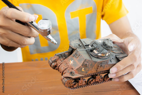 man painting scale model WW2 tank on table. Hobbie.