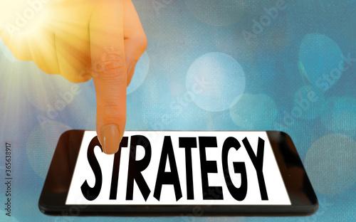 Writing note showing Strategy. Business concept for action plan or strategy designed to achieve an overall goal Modern gadgets white screen under colorful bokeh background