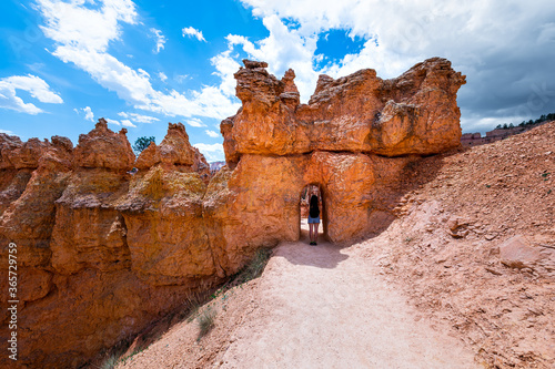 Young woman standing in desert landscape tunnel arch in Bryce Canyon National Park on Navajo loop Queen's Garden trail with sandstone rock formation