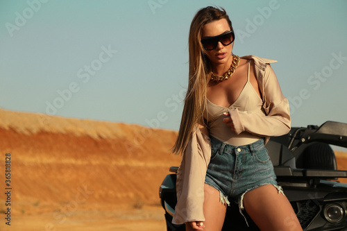 beautiful sexy woman with dark hair in casual clothes and accessories posing in desert with safari car