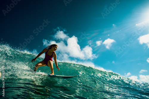 Professional Surfer Girl riding wave on surfing board under bright sun on background.