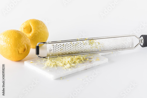 Lemon zest on a small marble slab with a microplane and two lemons to the left.