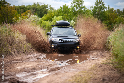 Black Subaru Forester moving at dirty forest road making a lot of water splashes