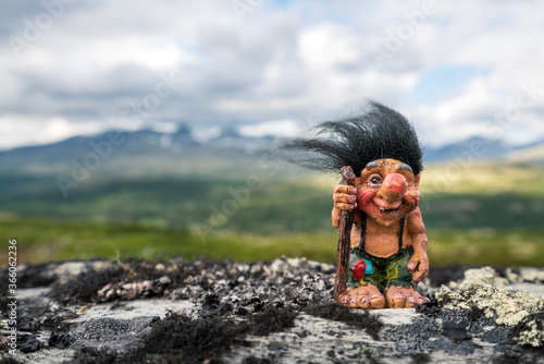 Funny norwegian troll figure with big nose and walking stick outdoors in the mountains. Hair standing up because of windy conditions.